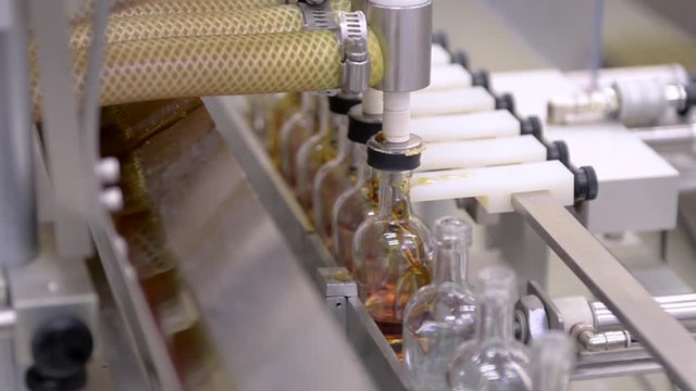 An assembly line machine fills glass bottles with maple syrup at a bottling plant.