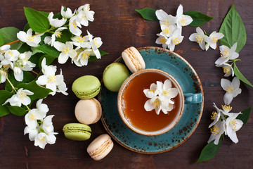 Fototapeta na wymiar Jasmine green tea with sweet french macarons, dark wooden table. Top view