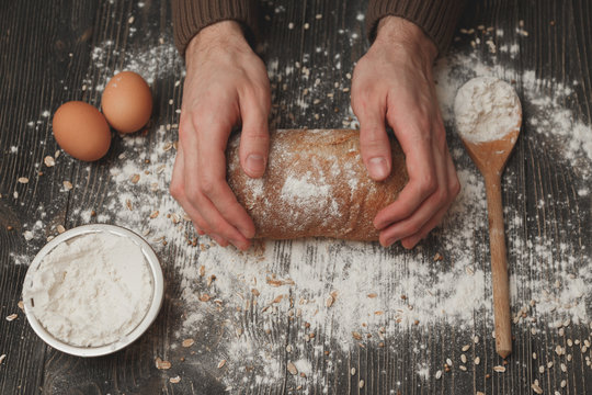 Close-up of men's hands on black bread with flour powder. Baking and patisserie concept.