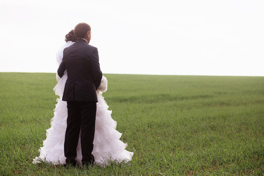 Bride and groom standing in a field picture from behind.