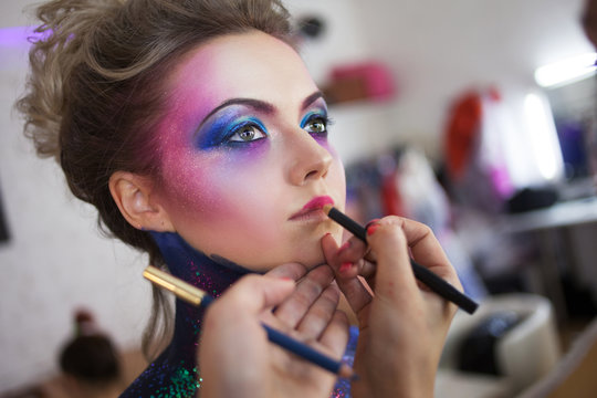 Makeup artist paints her lips. Young attractive blonde girl in bright art-makeup.