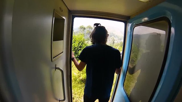 guy in the shirt rides the train standing at the door and holds onto the rail in Sri Lanka gopro