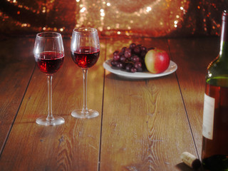 Two glasses of red wine and a plate with fruits on a wooden table and sparkling background