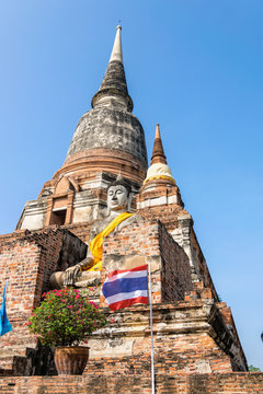 Buddha statue at the bottom of a large ancient pagoda on blue sky background at Wat Yai Chai Mongkon temple in Phra Nakhon Si Ayutthaya Historical Park, Ayutthaya Province, Thailand