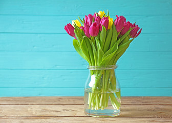 Glass vase with bouquet of beautiful tulips on wooden background