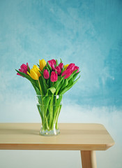 Glass vase with bouquet of beautiful tulips on color background