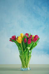 Glass vase with bouquet of beautiful tulips on color background