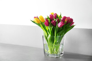 Glass vase with bouquet of beautiful tulips on color background