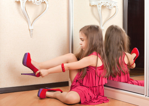 Little girl sitting on the floor, wearing adult shoes