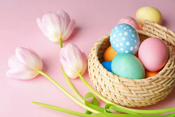 Fototapeta na wymiar Basket with painted Easter eggs and flowers on pink background