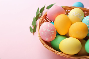 Basket with painted Easter eggs and green leaves on pink background