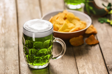 St. Patrick Day concept. Glass of green beer and plate with crisps on wooden table
