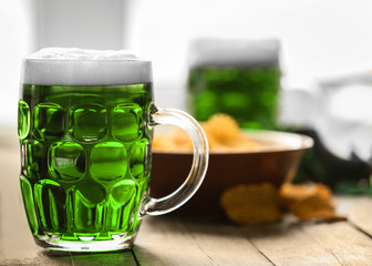 St. Patrick Day concept. Glass of green beer and plate with crisps on wooden table