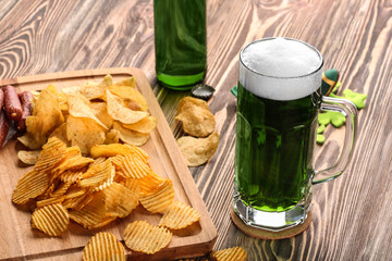 St. Patrick Day concept. Glass of green beer with crisps and sausages on wooden board, closeup