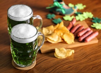 St. Patrick Day concept. Glasses of green beer and board with crisps and sausages on wooden table