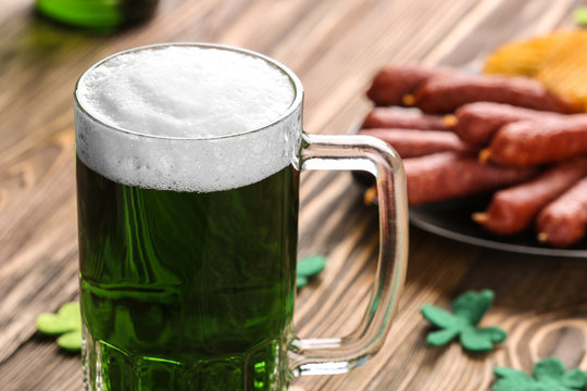 St. Patrick Day concept. Glass of green beer and plate with crisps and sausages on wooden table