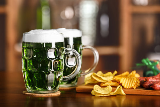 St. Patrick Day concept. Glasses of green beer and crisps on bar counter and blurred background