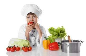 Cute boy in chef uniform with vegetables and saucepan on white background