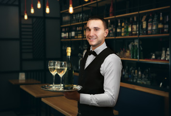 Young handsome waiter holding tray with wine glasses in the restaurant