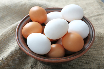 Bowl with raw eggs on fabric background