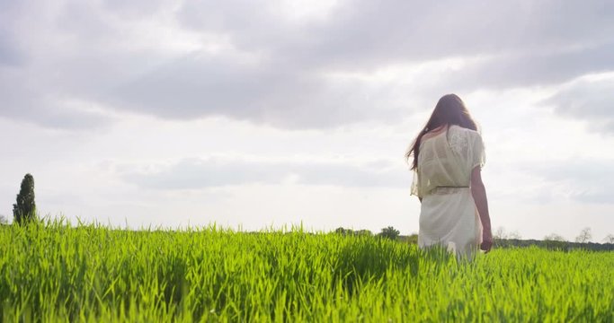 beautiful young woman admires the happy and carefree nature in a meadow at sunset in slow motion