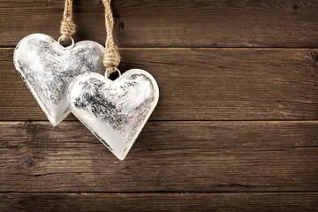 Two rustic metal heart ornaments hanging against a vintage wooden background