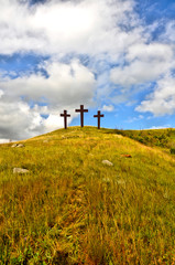 Obraz premium Three crosses on a grassy hill with a bright cloudy blue sky, to represent the crucifixion of Jesus. 