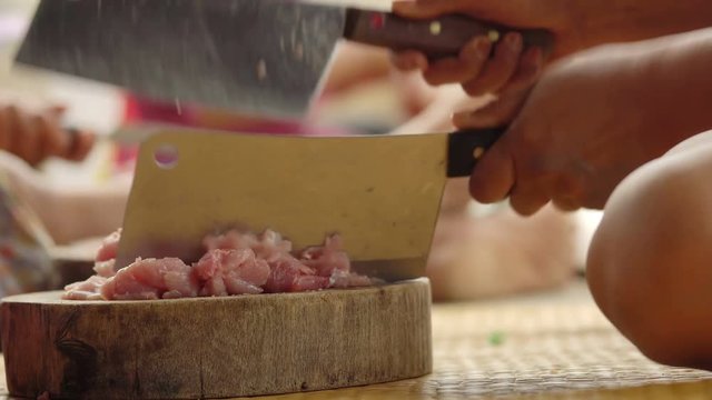 Pork mincing on a wooden chopping block with a cleaver
