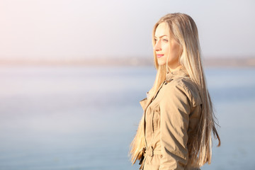 Beautiful young woman near river on sunny autumn day