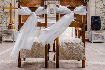 Fototapeta na wymiar Horizontal photo in color of a pair of main wedding chairs, holding a ribbon on a quarry chapel