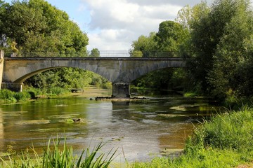 Fototapeta na wymiar Slow flowing river with age old archway bridge