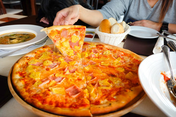 Woman's hand picked Hawaiian pizza from a wooden tray on the table.