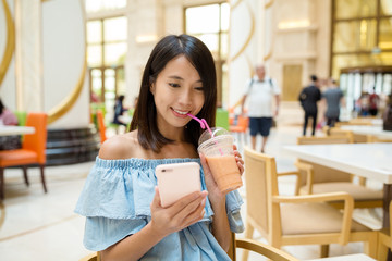 Woman looking and cellphone and drinking juice