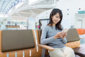 Woman using cellphone and sitting at departure hall
