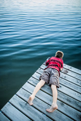 Fototapeta premium Boy laying on a dock looking at the water