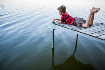 Boy laying on a dock by a lake