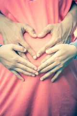 Pregnant Woman and Her Husband holding her hands in a heart shap