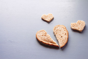 A broken heart on rustic wooden table with small hearts laying down on the table, shape of broken heart made from brown bread