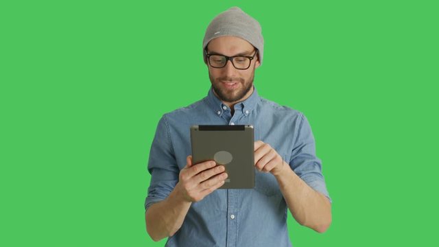 Mid Shot of a Stylish Man Wearing Hat and Glasses Using Tablet Computer. Background is Green Screen. Shot on RED Cinema Camera 4K (UHD).