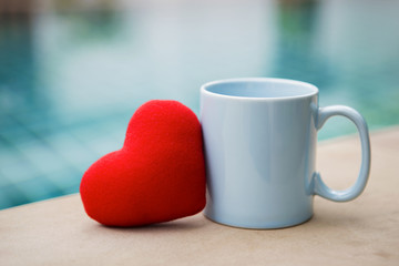 Red heart with blue coffee cup over swimming pool background