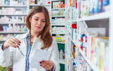 Woman pharmacist holding prescription checking medicine in pharmacy - drugstore.