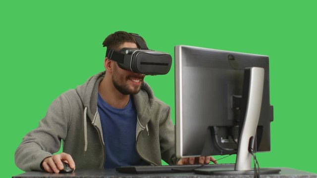 Mid Closeup Shot of a IT Man Wearing VR Headset Sitting at His Desktop Having Fun. Shot on a Green Screen  Background.  Shot on RED Cinema Camera 4K (UHD).