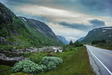 Obraz premium Norwegian river and road with dramatic sky at sunset