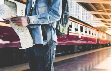 Fototapeta premium Backpacker waiting for long journey travel at train station with backpack and map on hand. Travel concept with vintage filter effected.
