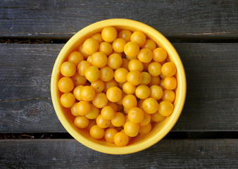 Yellow ripe plum in a round bowl on a brown wooden floor. Top view.