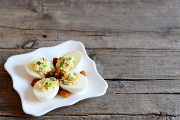 Deviled eggs on a white plate and on old wooden background with empty place for text. Hard-boiled eggs stuffed with cheese, marinated mushrooms and fresh green onion. Vegetarian appetiser recipe