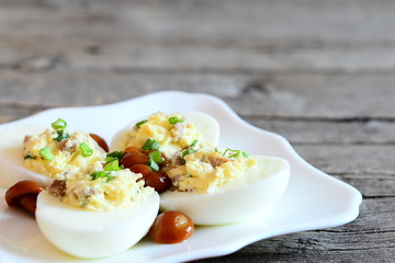 Tasty deviled eggs on a plate and on old wooden background with empty space for text. Hard-boiled eggs stuffed with cheese, marinated mushrooms and fresh green onion. Holiday starter recipe. Closeup