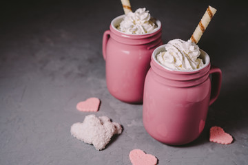 Two pink mugs with hot chocolate and cream on a gray concrete background. Drinks for a loving couple. The concept of Valentine's Day.