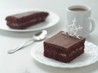 Piece of homemade chocolate cake decorated with sugar snowflake. Chocolate brownies arranged on white plate. Selective focus on the snowflake.