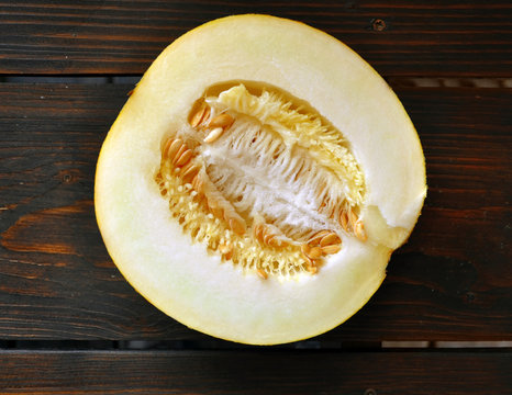 Half of ripe melon with seeds closeup on a dark wooden surface.